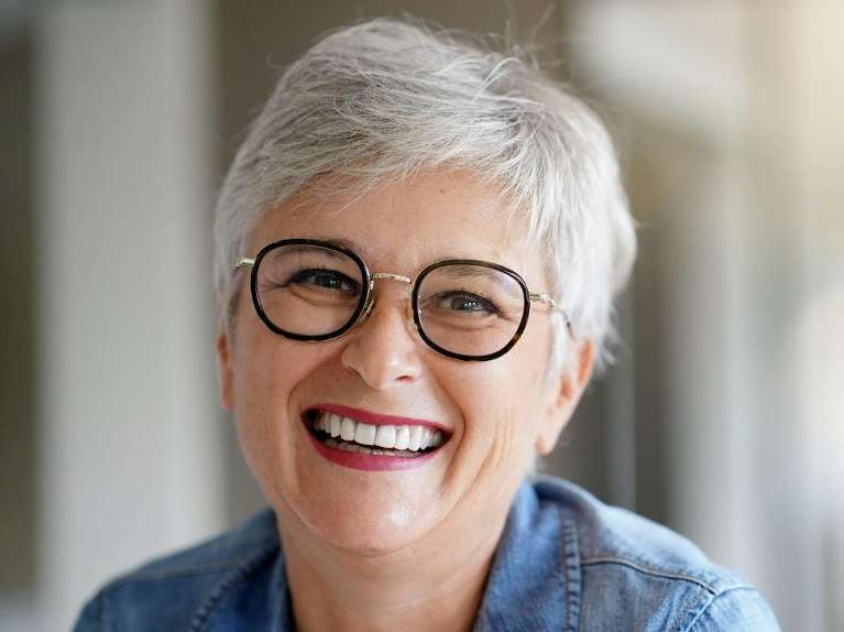 woman with black glasses smiling | dental bridges bloomington in