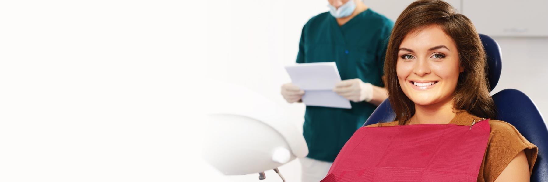 woman sitting in dental exam chair smiling l dental implants bloomington in
